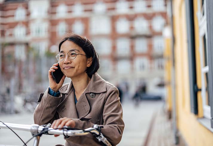 Ung asiatisk kvinde står på gaden med sin telefon og sin cykel